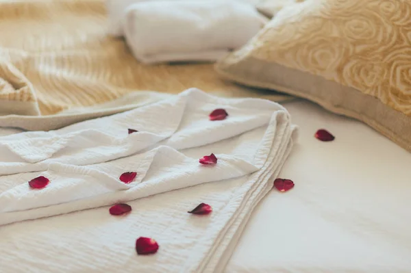 Luxury wellness and spa hotel room arranged for romantic weekend. Honeymoon suite bedroom decorated with rose petals on bed sheets. Resort holiday relaxation