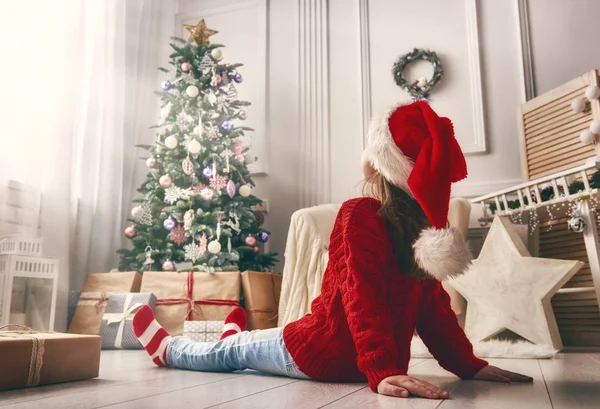Criança sentada perto da árvore de Natal dentro de casa — Fotografia de Stock