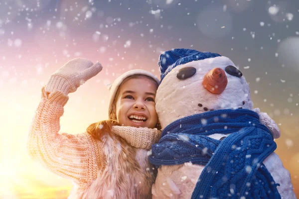 Flicka som leker med en snögubbe — Stockfoto