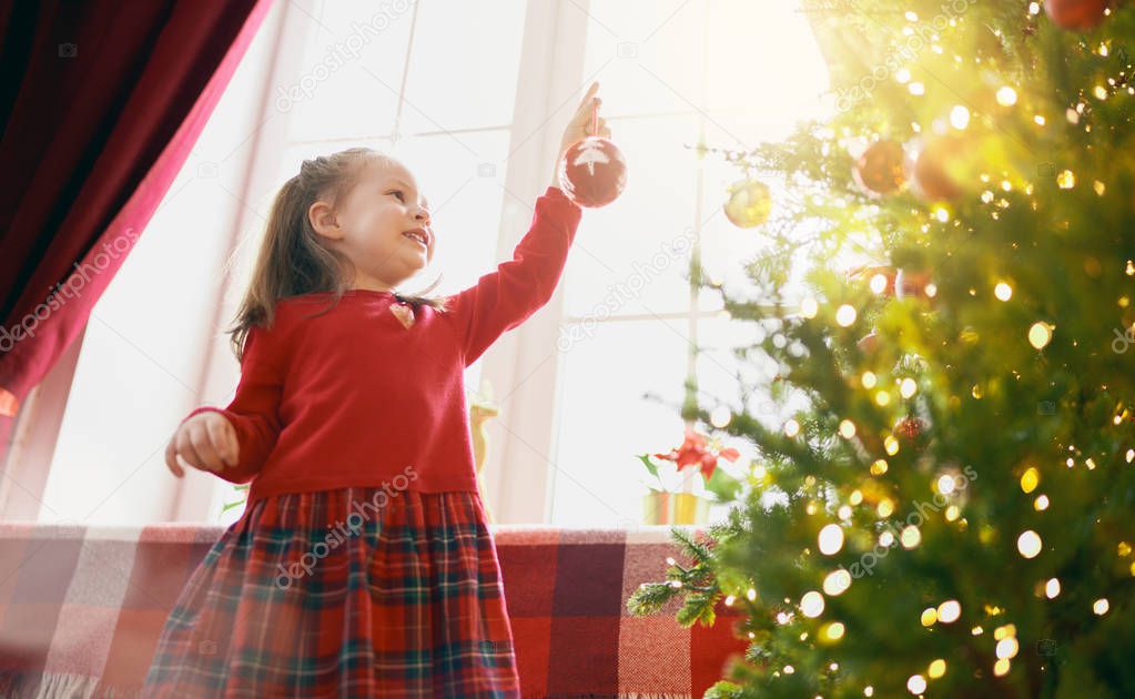 child with baubles near tree at home. 