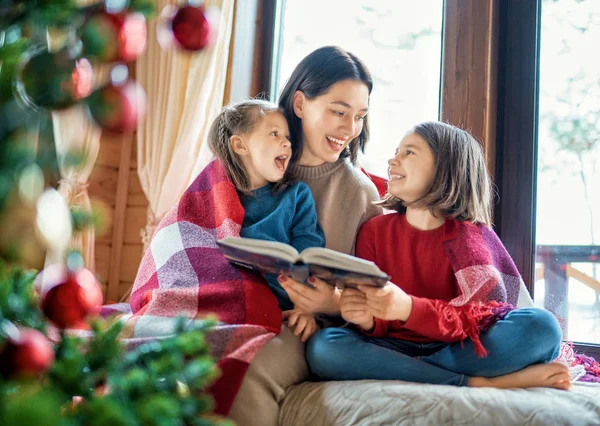 크리스마스 트리 근처에서 딸들에게 읽어 주는 엄마들. — 스톡 사진