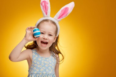 Tavşan kulakları Paskalya gününde giyen sevimli küçük çocuk. Parlak sarı zemin üzerine boyalı yumurta ile kız.                               