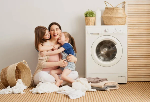 美しい若い女性と子供たちの女の子小さなヘルパーは家で洗濯をしながら楽しさと笑顔を持っています — ストック写真