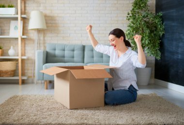 Güzel genç bir kadın elinde karton bir kutu tutuyor. Evdeki koltukta oturuyor.. 