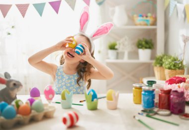 Güzel çocuk boyama yumurta. Mutlu bir aile Paskalya için hazırlanıyor. Sevimli küçük kız tavşan kulakları giyiyor.   
