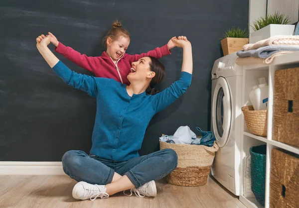 美しい若い女性と子供の女の子の小さなヘルパーは家で洗濯をしながら楽しさと笑顔を持っています — ストック写真