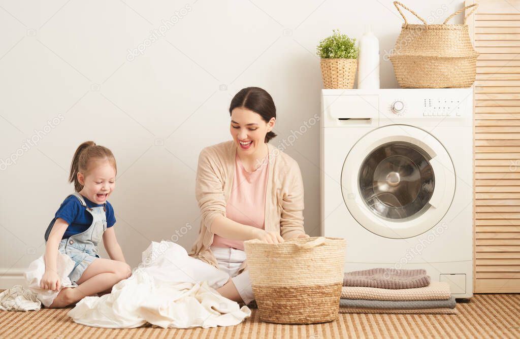 Beautiful young woman and child girl little helper are having fun and smiling while doing laundry at home.                                