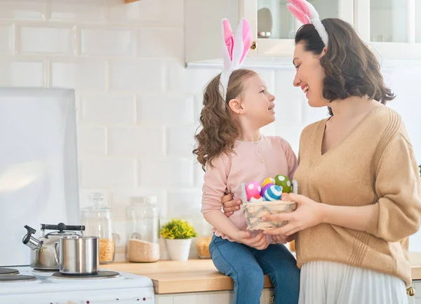 Happy holiday! A mother and her daughter are painting eggs. Family preparing for Easter. Cute little child girl is wearing bunny ears.