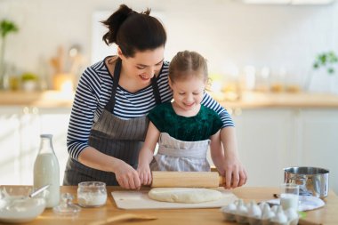 Mutlu aile birlikte fırın hazırlıyor. Anne ve kız çocuk kurabiye pişiriyor ve mutfakta eğleniyorlar. Ev yapımı yemek ve küçük bir yardımcı..                                
