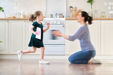 Anneler Günün kutlu olsun! Çocuk kızı annemi tebrik ediyor ve ona kartpostal veriyor. Anne ve kız gülümsüyor ve sarılıyorlar. Aile tatili ve birliktelik.                                