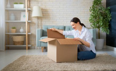 Güzel genç bir kadın elinde karton bir kutu tutuyor. Evdeki koltukta oturuyor.. 