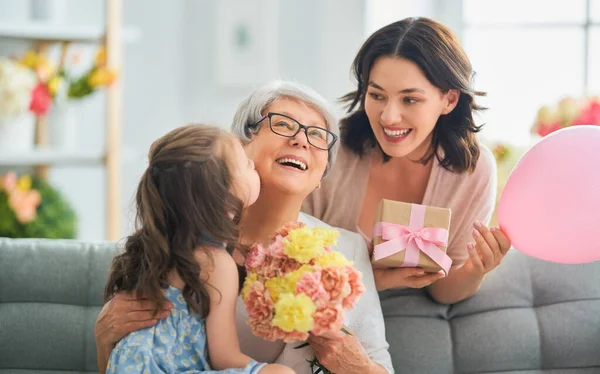 母亲节快乐 孩子的女儿在向妈妈和奶奶表示祝贺 向他们送花和礼物 妈妈和女孩笑着和拥抱 家庭假日和团聚 — 图库照片