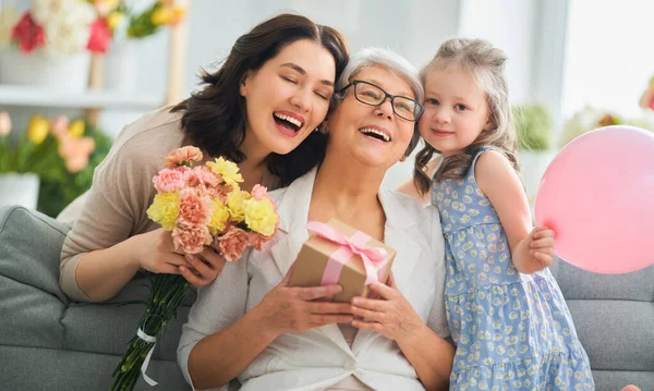 母亲节快乐 孩子的女儿在向妈妈和奶奶表示祝贺 向他们送花和礼物 妈妈和女孩笑着和拥抱 家庭假日和团聚 — 图库照片