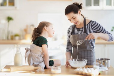 Mutlu aile birlikte fırın hazırlıyor. Anne ve kız çocuk kurabiye pişiriyor ve mutfakta eğleniyorlar. Ev yapımı yemek ve küçük bir yardımcı..                                