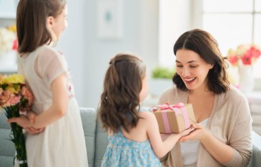 Anneler Günün kutlu olsun! Çocuklar annemi tebrik ediyor. Anne ve kızları gülümsüyor, ellerinde çiçekler ve hediyeler var. Aile tatili ve birliktelik.