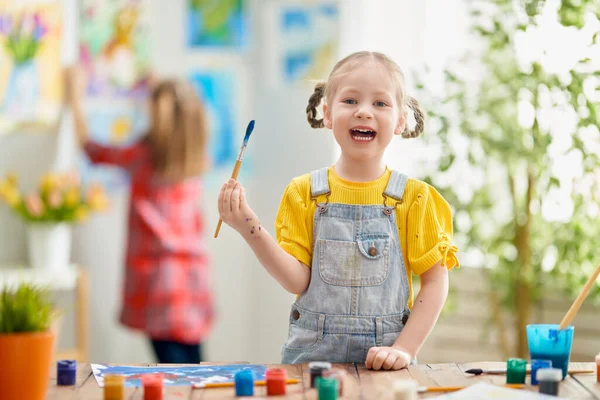 幸せな子供は家で絵を描いている 女の子は机の上に座って創造的な仕事をしています — ストック写真