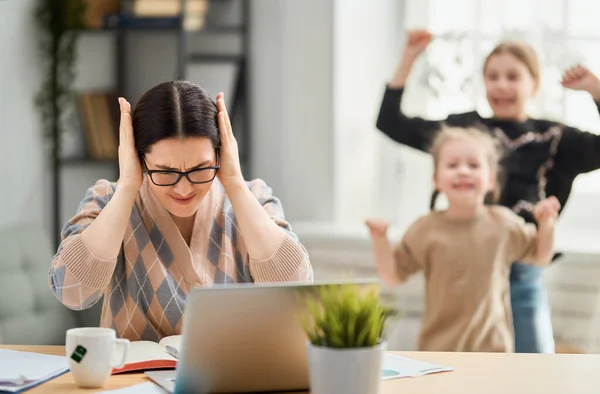 在笔记本电脑上工作的女人吵闹的儿童和离家遥远的工作 — 图库照片