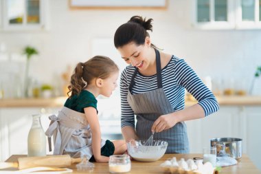 Mutlu aile birlikte fırın hazırlıyor. Anne ve kız çocuk kurabiye pişiriyor ve mutfakta eğleniyorlar. Ev yapımı yemek ve küçük bir yardımcı..                                