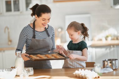 Mutlu aile birlikte fırın hazırlıyor. Anne ve kız çocuk kurabiye pişiriyor ve mutfakta eğleniyorlar. Ev yapımı yemek ve küçük bir yardımcı.. 