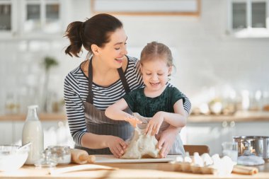 Mutlu aile birlikte fırın hazırlıyor. Anne ve kız çocuk kurabiye pişiriyor ve mutfakta eğleniyorlar. Ev yapımı yemek ve küçük bir yardımcı..                                