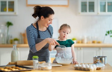 Mutlu aile birlikte fırın hazırlıyor. Anne ve kız çocuk kurabiye pişiriyor ve mutfakta eğleniyorlar. Ev yapımı yemek ve küçük bir yardımcı..                                