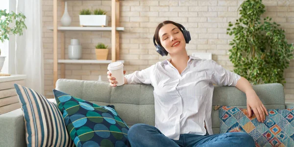 快乐的年轻女子坐在家里的沙发上 用耳机听着音乐 — 图库照片