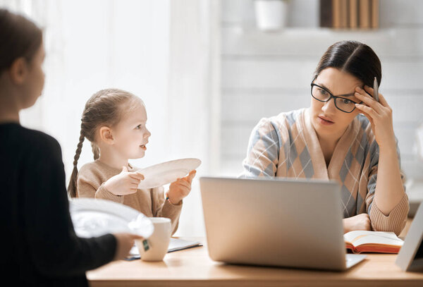 Woman working on a laptop. Noisy children and remote work from home.