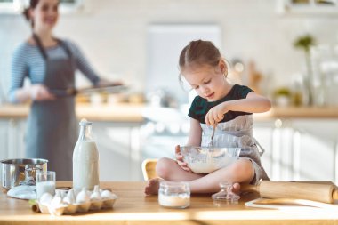 Mutlu aile birlikte fırın hazırlıyor. Anne ve kız çocuk kurabiye pişiriyor ve mutfakta eğleniyorlar. Ev yapımı yemek ve küçük bir yardımcı..   