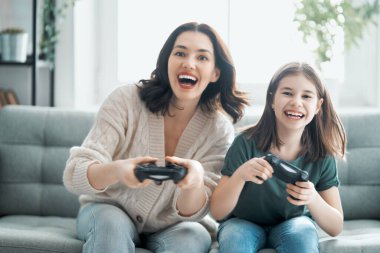 Mutlu aile birlikte. Anne ve kız çocuğu video oyunu oynuyorlar. İnsanlar evde eğleniyor..