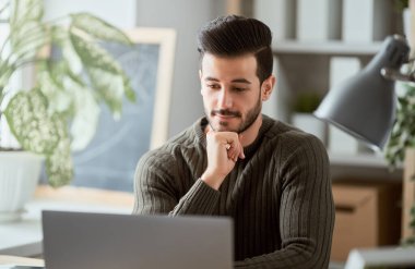 Evde dizüstü bilgisayarla çalışan mutlu bir genç adam..    