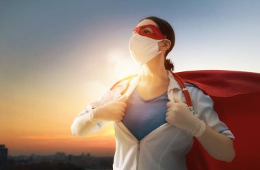 Koronavirüs salgını sırasında maskeli ve süper kahraman pelerinli bir doktor. Virüs ve hastalık koruması, karantina. COVID-2019. Tıbbın süper kahraman gücü. Günbatımı şehir planındaki kişi.