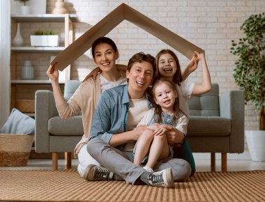 Anne, baba ve çocuk kızları çatı sembolü ile odasında. Genç aile konut kavramı.  