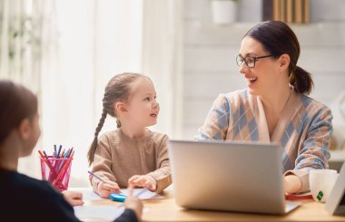 Bilgisayarda çalışan çocuklu genç bir anne. Aile evde. Uzak çalışma.                                