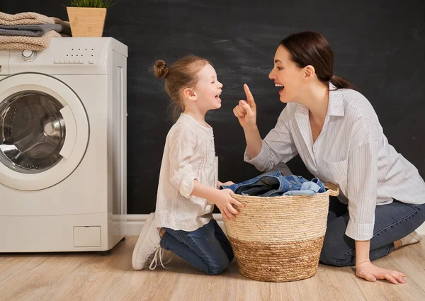 美しい若い女性と子供の女の子の小さなヘルパーは家で洗濯をしながら楽しさと笑顔を持っています — ストック写真