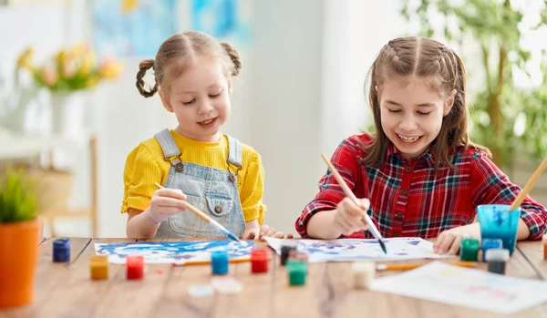 幸せな子供たちは家で絵を描いている 女の子たちは机の上に座って創造的な仕事をしています — ストック写真