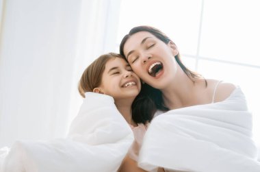 Hoş bir kız ve annesi güneşli bir sabahın tadını çıkarırlar. Evde iyi eğlenceler. Çocuk uykudan uyanıyor. Aile yatak odasında yatakta oynuyor.. 