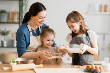 Mutlu aile birlikte fırın hazırlıyor. Anne ve çocuk kızları kurabiye pişiriyor ve mutfakta eğleniyorlar. Ev yapımı yemek ve küçük bir yardımcı..   