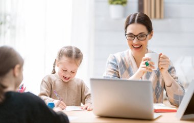 Bilgisayarda çalışan çocuklu genç bir anne. Aile evde. Uzak çalışma. 