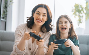 Mutlu aile birlikte. Anne ve kız çocuğu video oyunu oynuyorlar. İnsanlar evde eğleniyor..