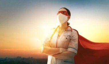 Koronavirüs salgını sırasında maskeli ve süper kahraman pelerinli bir doktor. Virüs ve hastalık koruması, karantina. COVID-2019. Tıbbın süper kahraman gücü. Günbatımı şehir planındaki kişi.