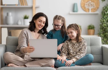 Sevgi dolu bir aile. Laptop kullanan genç anne ve kız çocukları. Komik anne ve güzel çocuklar evde kalarak eğleniyorlar.. 