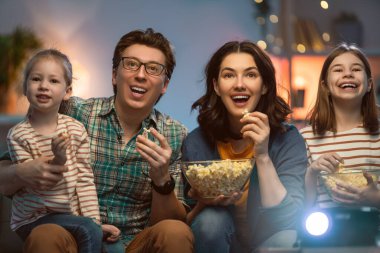 Mutlu aile projektörü, TV, akşam evde patlamış mısırlı filmler. Anne, baba ve kızları birlikte vakit geçiriyorlar..