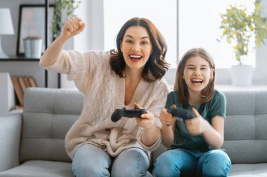 Mutlu aile birlikte. Anne ve kız çocuğu video oyunu oynuyorlar. İnsanlar evde eğleniyor..