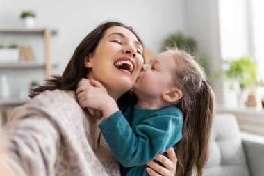 Sevgi dolu bir aile. Genç bir anne ve kız, arkadaşlarıyla ya da selfie çekmek için akıllı telefon kullanıyor. Komik anne ve güzel çocuk evde kalarak eğleniyorlar..