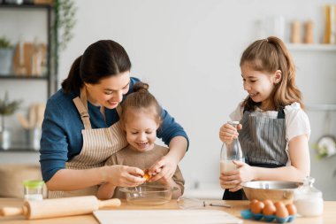 Mutlu aile birlikte fırın hazırlıyor. Anne ve çocuk kızları kurabiye pişiriyor ve mutfakta eğleniyorlar. Ev yapımı yemek ve küçük bir yardımcı.. 