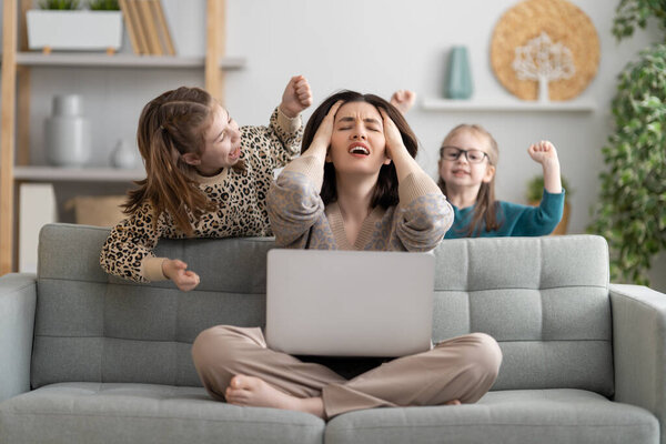 Woman working on a laptop. Noisy children and remote work from home.
