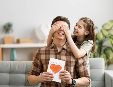 Babalar günün kutlu olsun! Çocuk kızı babasını tebrik ediyor ve ona kartpostal veriyor. Baba ve kız gülümsüyor ve sarılıyorlar. Aile tatili ve birliktelik.