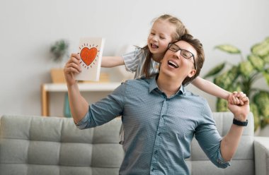 Babalar günün kutlu olsun! Çocuk kızı babasını tebrik ediyor ve ona kartpostal veriyor. Baba ve kız gülümsüyor ve sarılıyorlar. Aile tatili ve birliktelik.