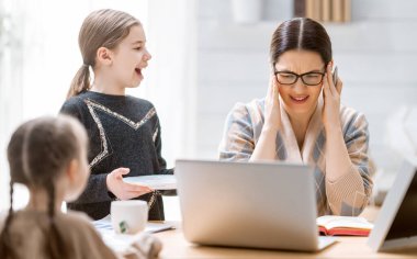 Dizüstü bilgisayarda çalışan bir kadın. Gürültülü çocuklar ve evden uzak çalışma.  