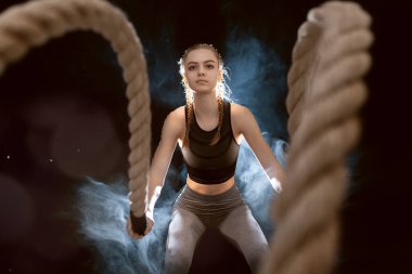 Atletik genç kadın koyu arkaplanda bir iple çapraz egzersizler yapıyor..